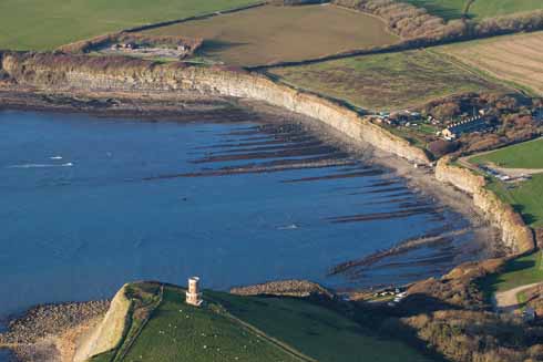 The characteristic seaward lines of Kimmeridge Bay with the Landmark Trust's Clavell Tower, which is available for holiday lets, in the foreground. It was disassembled from the edge of the crumbling cliff and rebuilt 25 metres further inland. In the distance is a nodding donkey oil pump.