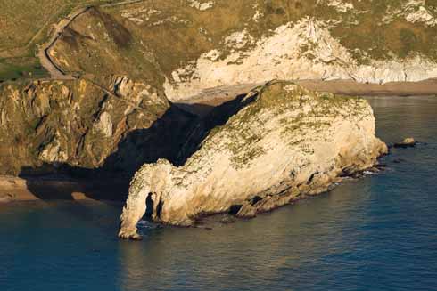 Durdle Door shot under raking side light that shows the once horizontal strata that make up the iconic rock formation having been thrust upwards to a near vertical aspect