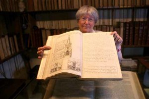 Librarian Judith Monds holding the history of Wimborne Minster open at the page showing the spire that used to sit atop one of the Minster's towers  